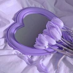 a heart shaped mirror sitting on top of a bed next to purple tulips