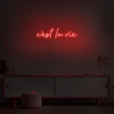 a red neon sign that reads est la vie on the wall above a white cabinet