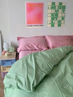 a bed with pink and green comforters in a white room next to a nightstand