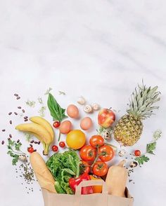 a bag full of fresh fruits and vegetables on a white table with a marble background