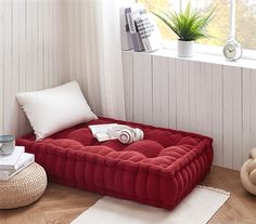 a red couch sitting on top of a wooden floor next to a window