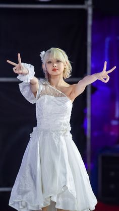 a woman in a white dress on stage with her hands up and two fingers out