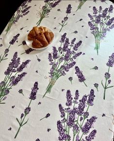 a table topped with purple flowers and pastries on top of it next to a bowl of croissants