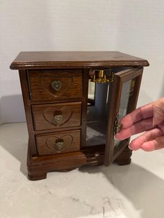 a hand is reaching into a small wooden cabinet with two drawers and one door open