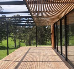 a wooden deck with glass walls and trees in the backgrouds, overlooking a grassy area