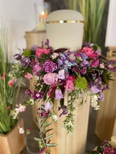 a vase filled with lots of purple flowers on top of a wooden table next to potted plants