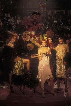 three women dressed in gold and black posing for a photo with an old piano behind them