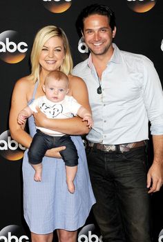 a man and woman holding a baby in front of a tv screen with the caption's name on it