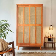 a wooden cabinet sitting in the corner of a living room next to a chair and table