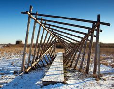 a wooden bridge in the middle of a snowy field with snow on the ground and blue sky