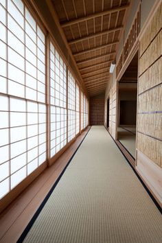 an empty hallway with lots of windows and wood paneling on the walls, leading to another room