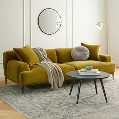 a living room with a yellow couch, round mirror and rug on the floor in front of it