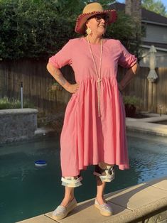 a woman standing on the edge of a pool wearing a pink dress and hat