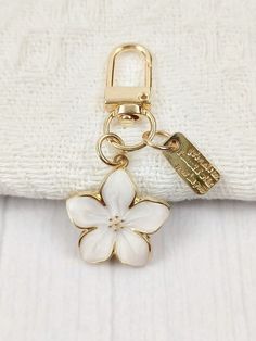 a white and gold keychain with a flower charm on it's side