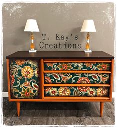 two lamps sitting on top of a wooden dresser next to a wall with the words t kay's creations