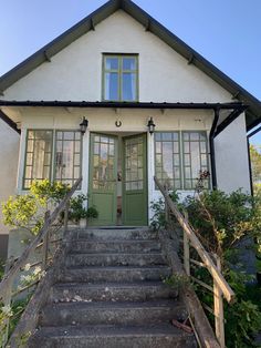 a house with stairs leading up to the front door and green doors on both sides