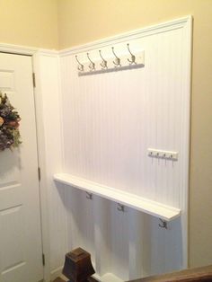 a white coat rack with hooks on the wall next to a wooden bench and door