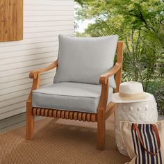 a wooden chair sitting on top of a rug next to a white wall and trees