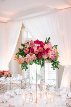 a tall vase filled with lots of pink and red flowers on top of a table