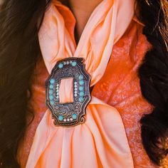 a woman wearing an orange scarf with a metal buckle on her neck and long black hair