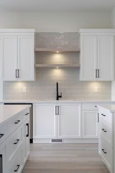 an empty kitchen with white cabinets and black handles on the countertop, along with wood flooring