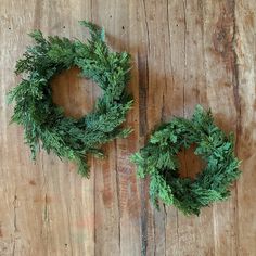 two green wreaths sitting on top of a wooden table next to each other,