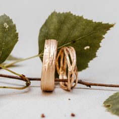 two gold wedding rings sitting on top of leaves