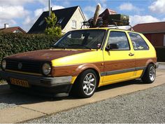 a yellow van with luggage on top parked in front of a house next to a hedge