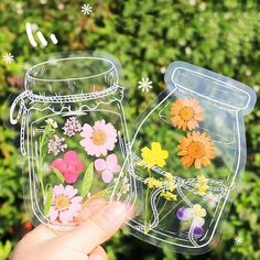 a hand holding up a clear sticker with flowers in the jar and another flower inside