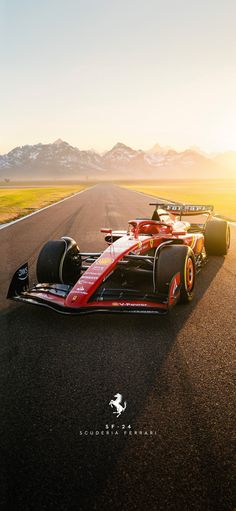 a red and black race car driving down a road with mountains in the background at sunset