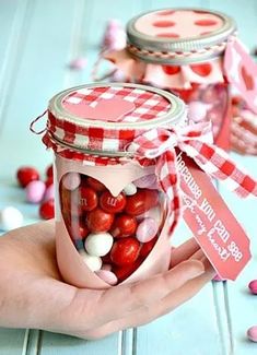 a hand holding a jar filled with red and white candies on top of a table