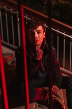 a young man sitting on the ground with his hand under his chin and looking at the camera