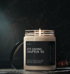 a candle sitting on top of a table next to a black mug with the words it's giving