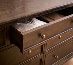 a wooden dresser with two white dishes in the drawer and an empty napkin on top