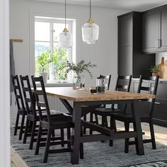 a dining room table and chairs in front of an open kitchen area with black cabinets