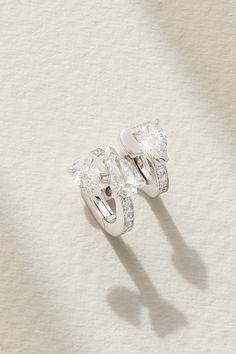 two diamond rings sitting on top of a white surface with shadows from the light coming through them