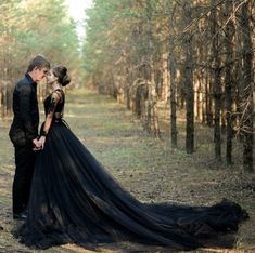 a man and woman dressed in black standing next to each other on a forest path