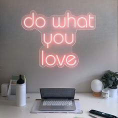 a laptop computer sitting on top of a desk next to a neon sign that says do what you love