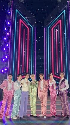 group of young men standing on stage with neon lights in the background and stars all around them