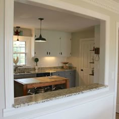 a kitchen with white cabinets and granite counter tops in the middle of it is seen through an open doorway