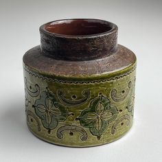 a green and brown vase sitting on top of a white table