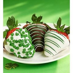 three chocolate covered strawberries on a white plate with shamrock decorations and green sprinkles