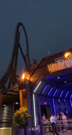 a roller coaster at night with people standing around it and the sign velocium