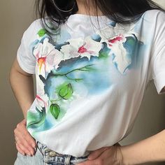 a woman wearing a white shirt with flowers painted on the front and back of it