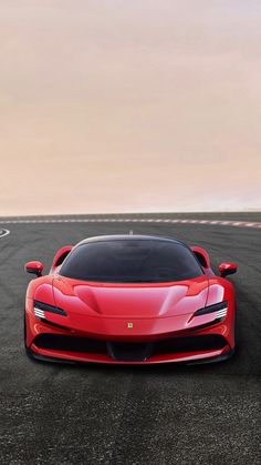 a red sports car driving on a race track in front of a white and gray sky