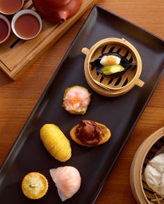 an assortment of sushi on a black platter next to other dishes and utensils