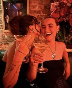 two women sitting next to each other holding wine glasses in front of their faces and smiling