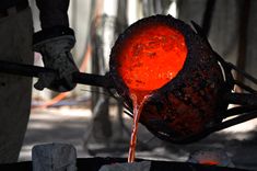 an orange substance is pouring out of a metal pot onto a black object with red liquid coming out of it