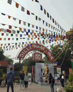 people are standing in front of an arch with flags hanging above it and there is a statue on the other side