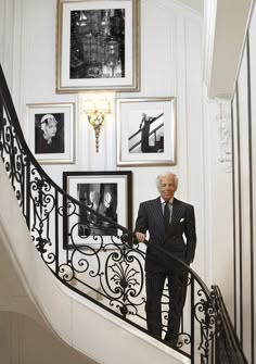 an old man in a suit is standing on the stair railing next to some pictures